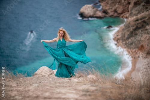 A woman in an emerald dress  a fashion model with long silk wings in a flowing dress  flying fabric on the embankment.