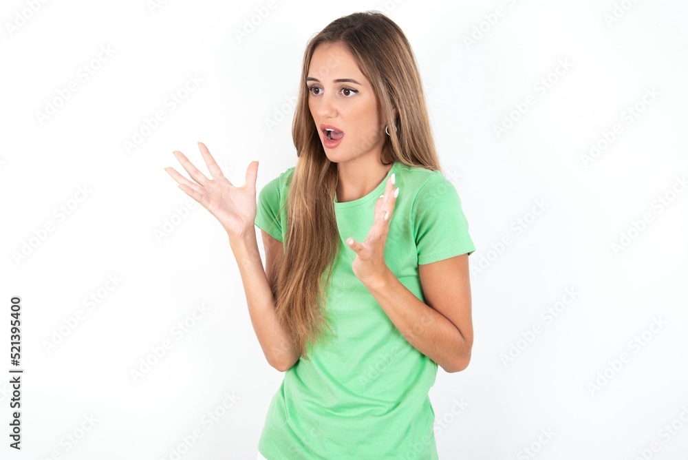 young beautiful woman wearing green T-shirt over white background, shouts loud, keeps eyes opened and hands tense. young beautiful woman wearing green T-shirt over white background, shouts loud, keeps eyes opened and hands tense.