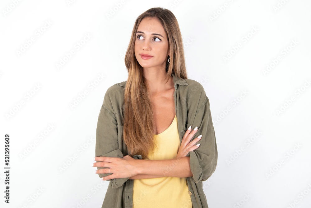 Charming thoughtful young beautiful woman wearing green overshirt over white background stands with arms folded concentrated somewhere with pensive expression thinks what to do Charming thoughtful young beautiful woman wearing green overshirt over white background stands with arms folded concentrated somewhere with pensive expression thinks what to do
