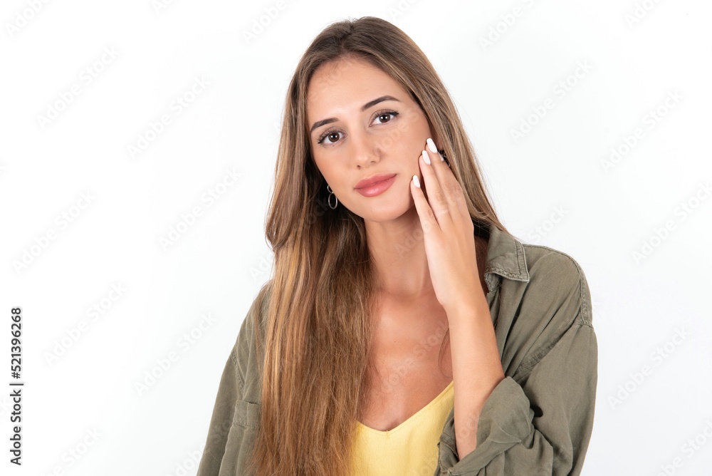 Photo of young beautiful woman wearing green overshirt over white background enjoy fresh perfect smooth skin touch face Photo of young beautiful woman wearing green overshirt over white background enjoy fresh perfect smooth skin touch face