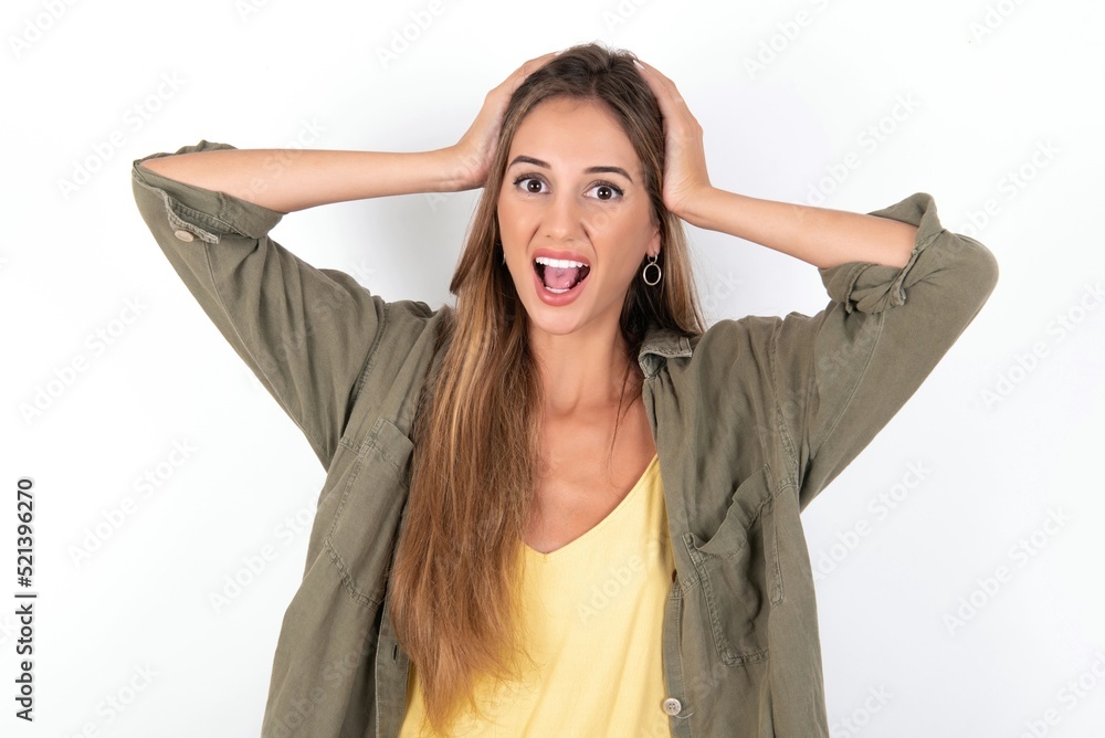 Cheerful overjoyed young beautiful woman wearing green overshirt over white background reacts rising hands over head after receiving great news. Cheerful overjoyed young beautiful woman wearing green overshirt over white background reacts rising hands over head after receiving great news.