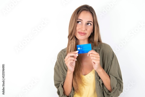 Photo of cheerful young beautiful woman wearing green overshirt over white background hold debit card look empty space photo