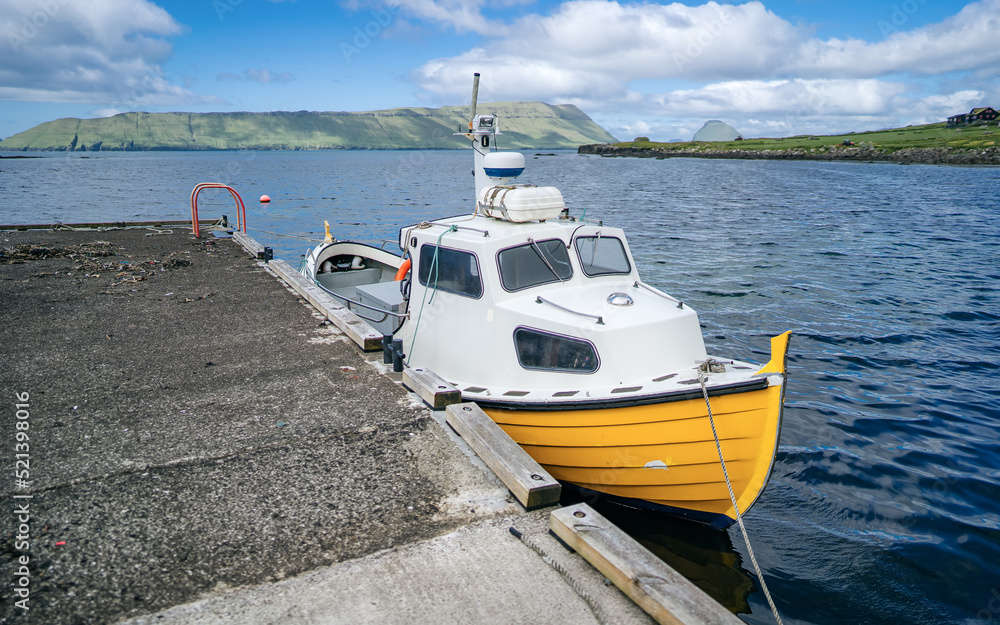 Fototapeta premium Fishing boat on a calm at the small harbor of the village of Kirkjubour, famous for the ruins of an ancient cathedral, Kirkjubomururin, on the island of Streymoy. Faroe islands