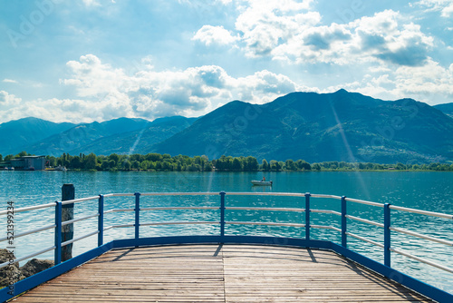 Old wooden jetty on the promenade of Lovere, Lake Iseo, Italy, with turquoise waters. Italian alps on the background, with blue sky and white clouds. © Travelling Jack