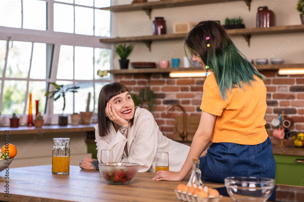 Fototapeta premium Very charismatic and good looking lesbian couple have a great time together in a large modern kitchen they discussing together and smiling large