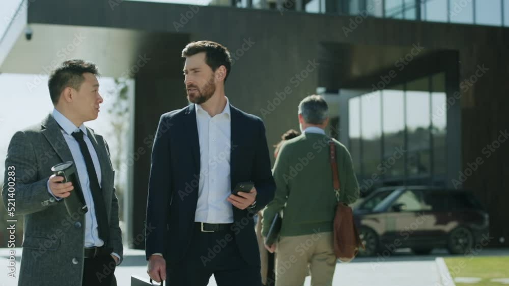 Handsome two business men walking talking discussing on street in modern city near business center. Use phone hold cup of coffee. People around. Portrait. Slow motion Handsome two business men walking talking discussing on street in modern city near business center. Use phone hold cup of coffee. People around. Portrait. Slow motion