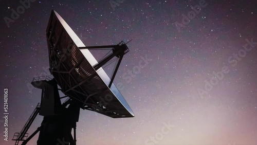 The silhouette of a massive earth-based space observatory satellite telescope scanning the night sky.