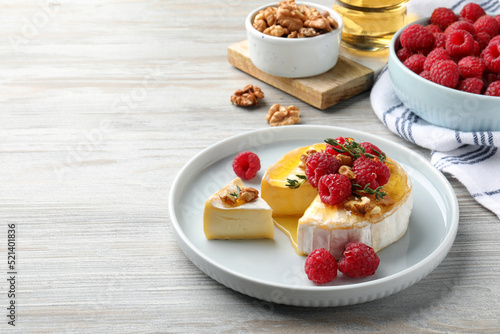 Brie cheese served with raspberries  walnuts and honey on white wooden table. Space for text