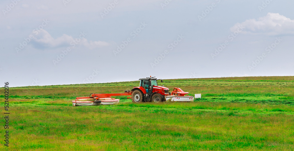 A red tractor mows the grass on a farmer's field. Two mowers will mow a large area of the field. A red tractor mows the grass on a farmer's field. Two mowers will mow a large area of the field.