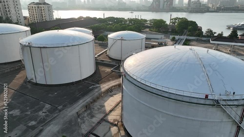 Oil storage tanks in rows along the riverside. Drone aerial view. Oil storage tanks in the sunset time, flying over the tanks along the river.  Industry, business, economy concept b-roll footage.
