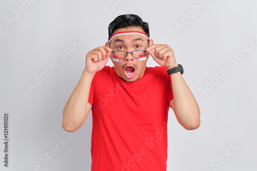 Shocked young Asian man celebrating Indonesian independence day take off glasses isolated on white background