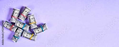 Rolled up one hundred dollar bills with rubber bands on purple background with copy space