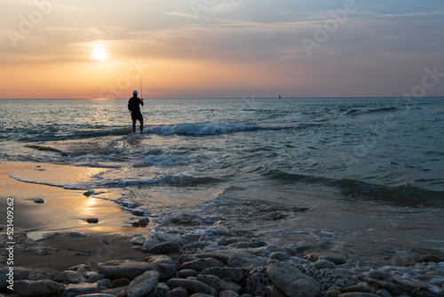 Unrecognizable young man fishing in a spectacular sunset. Adventure, outdoors, nature and ocean.