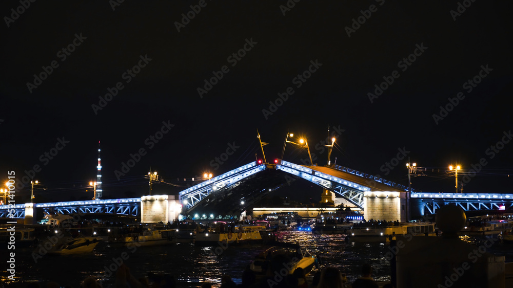 Building bridges with boat traffic at night. Action. Beautiful bridge construction with lighting at night. Many boats on river are waiting for breeding of luminous bridge