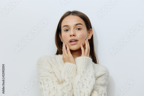 a close portrait of a pleasant, attractive young woman on a light background in a knitted sweater smiling gently at the camera with her hands folded around her neck