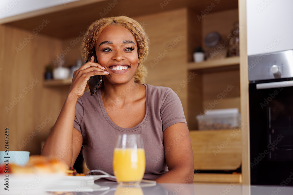 Woman having phone conversation and eating breakfast at home