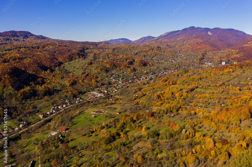 Aerial drone view of autumn landscape with houses on a sunny day near the Fagaras mountains.