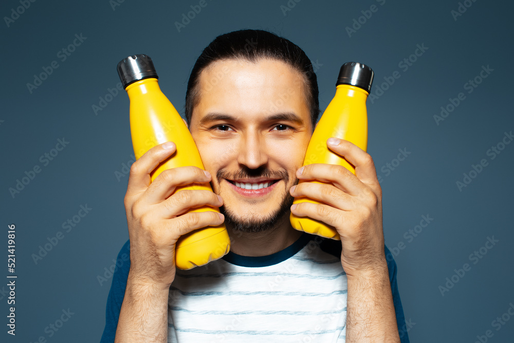 Studio portrait of young joyful man, holding two yellow eco bottles close to his face. Studio portrait of young joyful man, holding two yellow eco bottles close to his face.