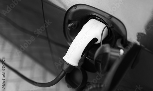 Plug-in hybrid EV car charging at charge station, home. Black and white photo. Close-up view.