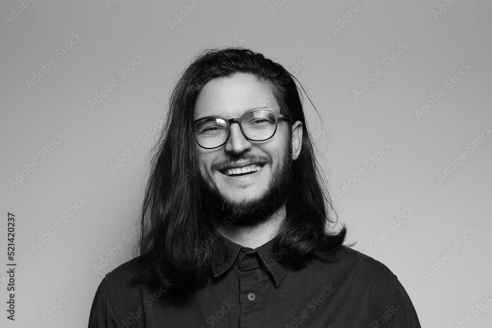 Black and white studio portrait of happiness man with long hair, smiling, wearing eyeglasses. Black and white studio portrait of happiness man with long hair, smiling, wearing eyeglasses.