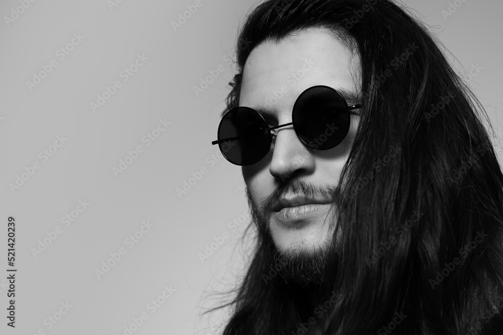 Black and white studio portrait of young serious man with long hair, wearing round sunglasses. Copy space concept. Black and white studio portrait of young serious man with long hair, wearing round sunglasses. Copy space concept.