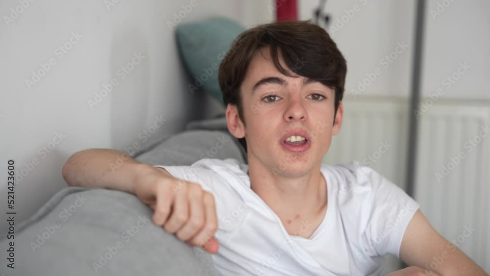 Teenager boy talking and looking at camera sitting on couch.