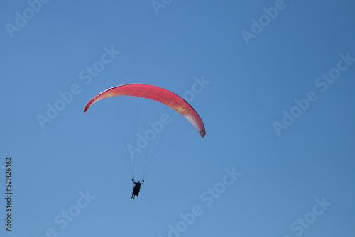 Parapente rouge dans un ciel bleu : préparation à l'atterrissage