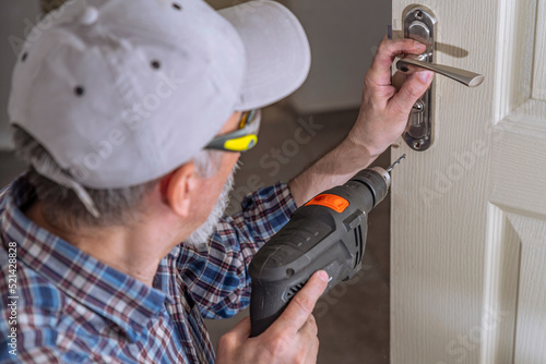 Door lock installation, repair, or replacement service. Door hardware installer locksmith working with open white door indoor photo