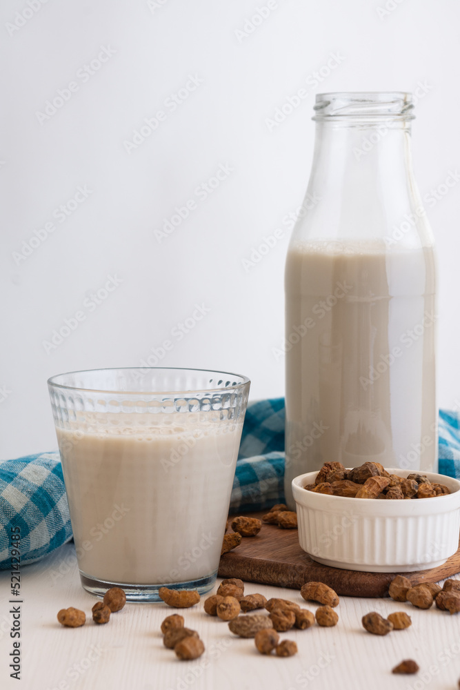 View of bottle and glass with horchata and tiger nuts on blue cloth, selective focus, white background, vertical, with copy space View of bottle and glass with horchata and tiger nuts on blue cloth, selective focus, white background, vertical, with copy space