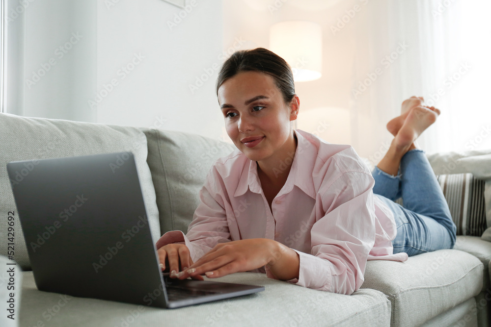 Close up shot of young woman working remotely from home on laptop, lying on the blue couch in living room. Female freelancer with hands on keyboard. Copy space, background Close up shot of young woman working remotely from home on laptop, lying on the blue couch in living room. Female freelancer with hands on keyboard. Copy space, background