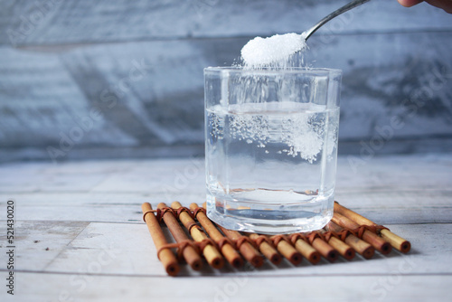 pouring white sugar in a glass of water on table  photo