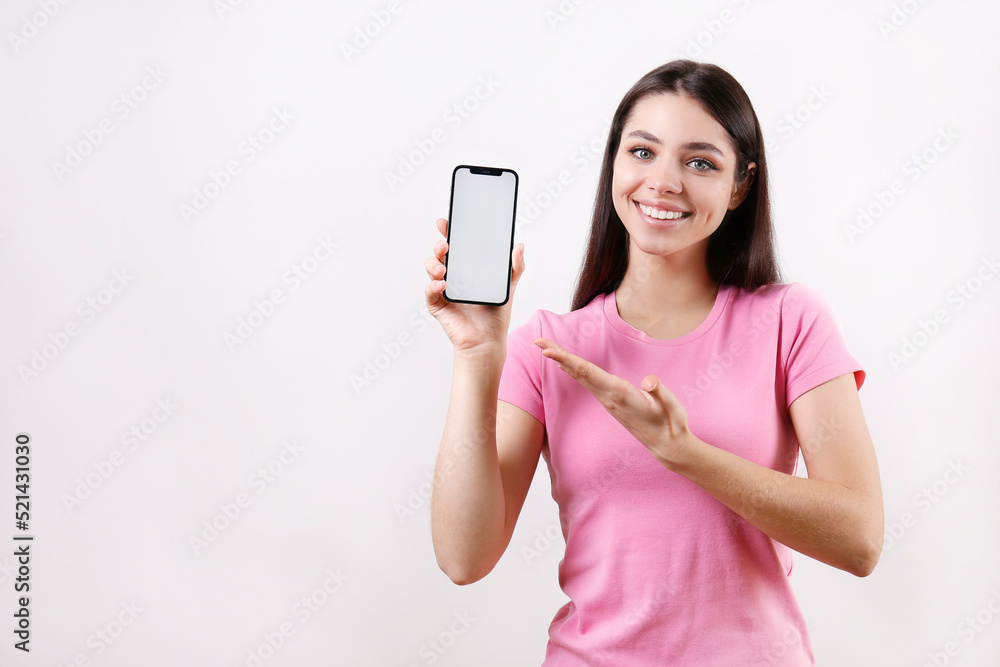 Young brunette woman wearing pink t-shirt, pointing at a phone over isolated background. Portrait of female model showing blank screen cellphone. Close up, copy space Young brunette woman wearing pink t-shirt, pointing at a phone over isolated background. Portrait of female model showing blank screen cellphone. Close up, copy space
