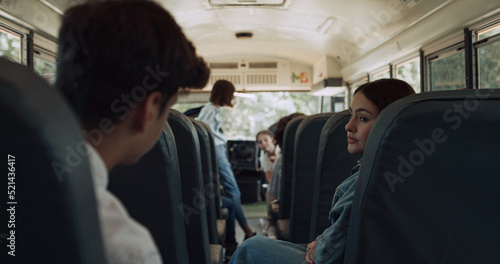 High school students sitting communicating in schoolbus. Pupils waving friend.