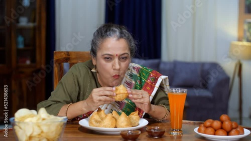 An aged Indian housewife eating Samosa - Indian street food  deep-fried  stuffed samosa  unhealthy food  trans fat  oily food. An old Indian lady bingeing on unhealthy food - poor lifestyle  cheat day photo