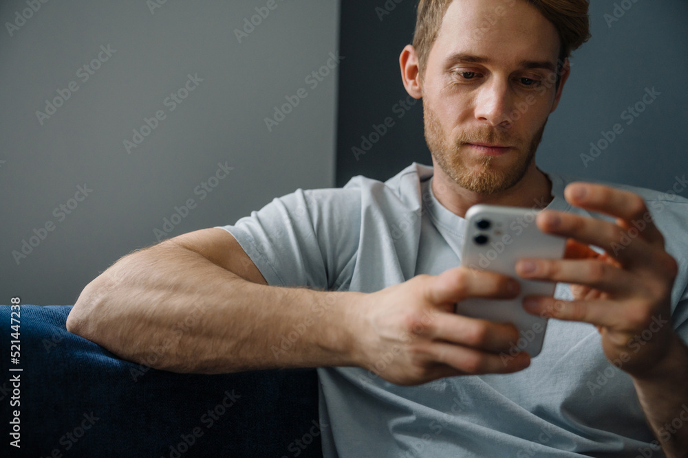 Young bearded man using cellphone while sitting on sofa at home Young bearded man using cellphone while sitting on sofa at home