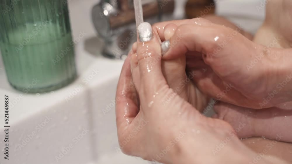 Close-up mother hand washing baby heel in a bathroom sink under tap. Child bathing in bathroom sink. Little toddler routine. Hygiene and skin care for children. 4K