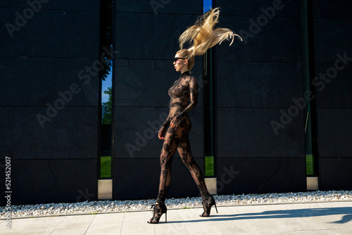 High fashion look. Glamour stylish model in black latex clothing and and high heels on is walking in the city. Sexy blonde woman in bodystocking lingerie is posing outdoor. Sexy Lingerie model.