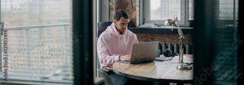 A young man works alone in the office with a laptop. Handsome guy sits at a table, works at a computer