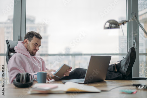 A young man works alone in the office with a laptop. A handsome guy sits at a desk, works at a computer