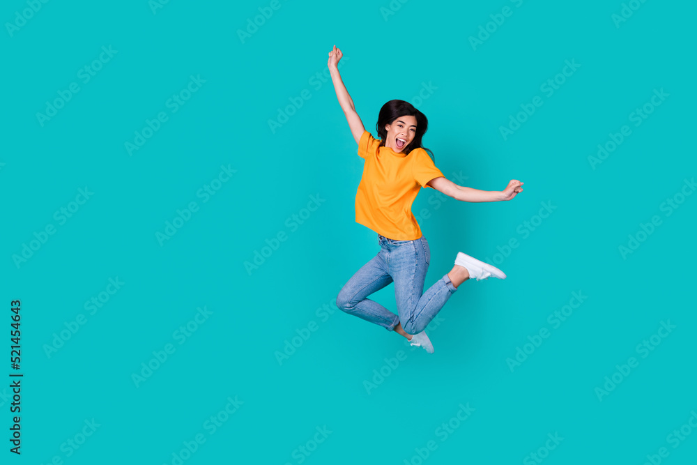 Full body photo of funky brunette lady jump wear orange t-shirt jeans boots isolated on teal color background Full body photo of funky brunette lady jump wear orange t-shirt jeans boots isolated on teal color background