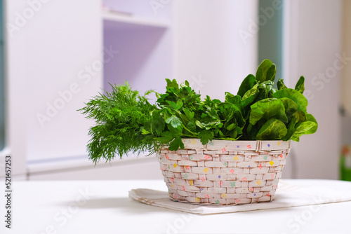 Isolated fresh juicy greens, dill, parsley, spinach, arugula in a wicker basket on a white table. Healthy nutrition. Vitamins, minerals. Balanced diet. Dietary supplement. Harvest. Organic gardening.