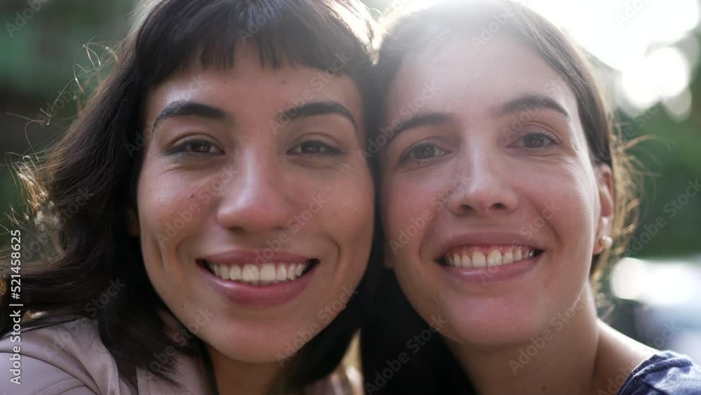 Two female friends together looking at camera. Portrait of diverse girls outside with sun flare Two female friends together looking at camera. Portrait of diverse girls outside with sun flare