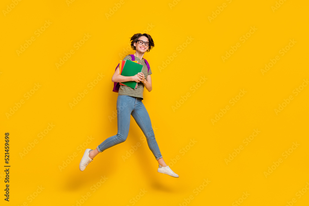 Full length photo of pretty sweet lady wear striped t-shirt spectacles backpack jumping empty space isolated yellow color background