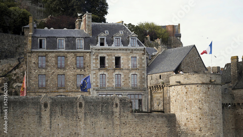 Amazing old brick house on the rock surrounded by high brck wall and a tower with tourists, architecture concept. Action. Ancient stony building with the flags of France, Europeen Union and Normandy. photo