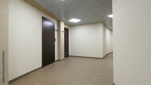 Empty, round corridor with light beige walls and closed, dark brown doors. Closed doors along a lighted corridor in the office building.