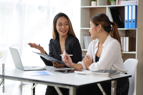 Attractive Asian businesswoman and secretary colleague discussing working on a business project at an office desk.