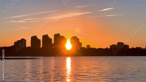 Beautiful sunset over a city with calm water in the foreground with a motorboat going on a lake. Boat goes from left to right