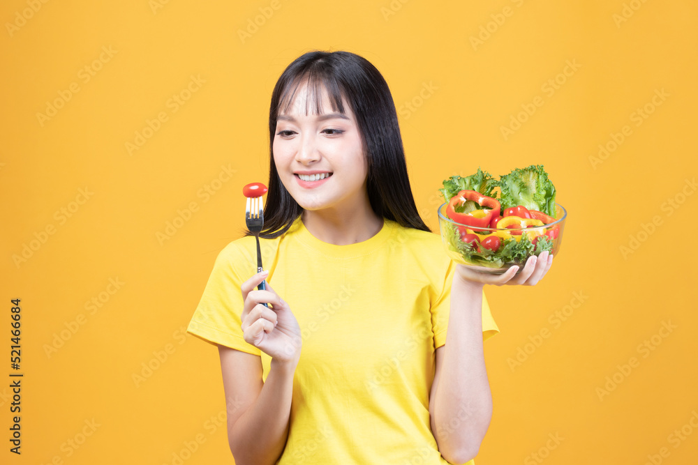 Portrait of happy asian woman eating tasty fresh vegetable salad holding plate bowl and fork on yellow background. Portrait of happy asian woman eating tasty fresh vegetable salad holding plate bowl and fork on yellow background.