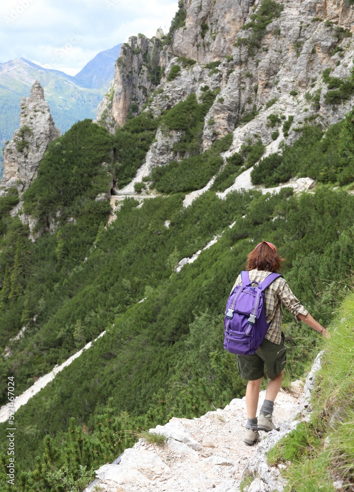 girl with backpack walks along a high mountain trail in northern Italy on the Dolomites