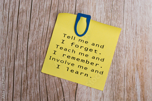 Motivational quote on yellow stick note on wooden table with blue paperclip.